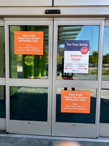 A view of the entrance doors at Mark Craft's hospital, where he goes for cancer treatment. The doors have signs related to COVID-19 warnings.