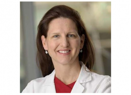Headshot of Dr. Kathryn Beal, a new Board Member. She is wearing a white coat with red shirt underneath, and has long brown hair, and is facing forward while smiling.