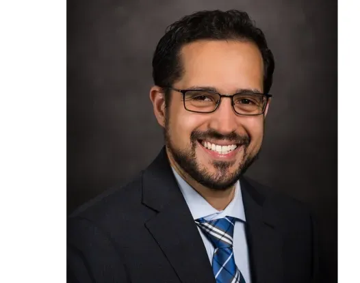 Dr. Pavlos Msaouel headshot; he is smiling facing forward against a dark-gray background.