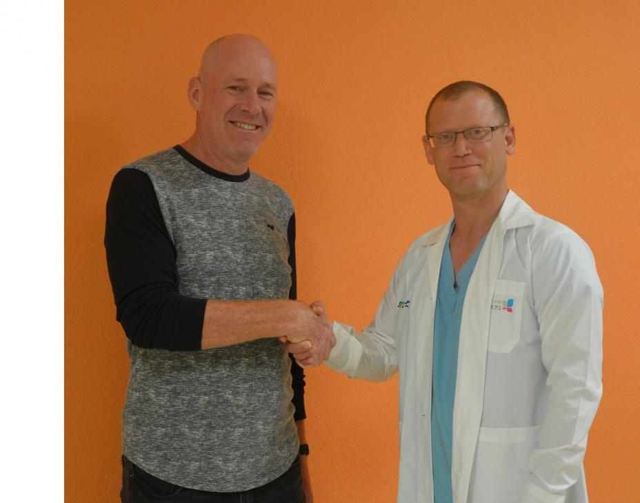 Dr. David Margel shaking hands with his patient, Uriya, in front of orange background.