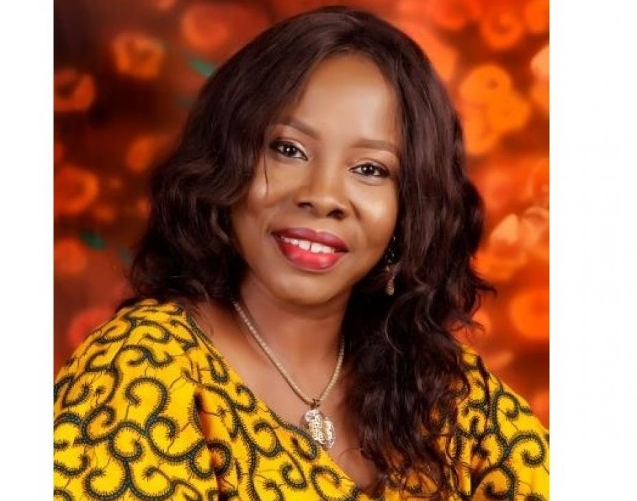 Headshot of Dr. Tonia Onyeka smiling. Background is bright, deep orange. Dr. Onyeka is wearing a gold-colored long-sleeve shirt with an intricate pattern colored dark brown to black.