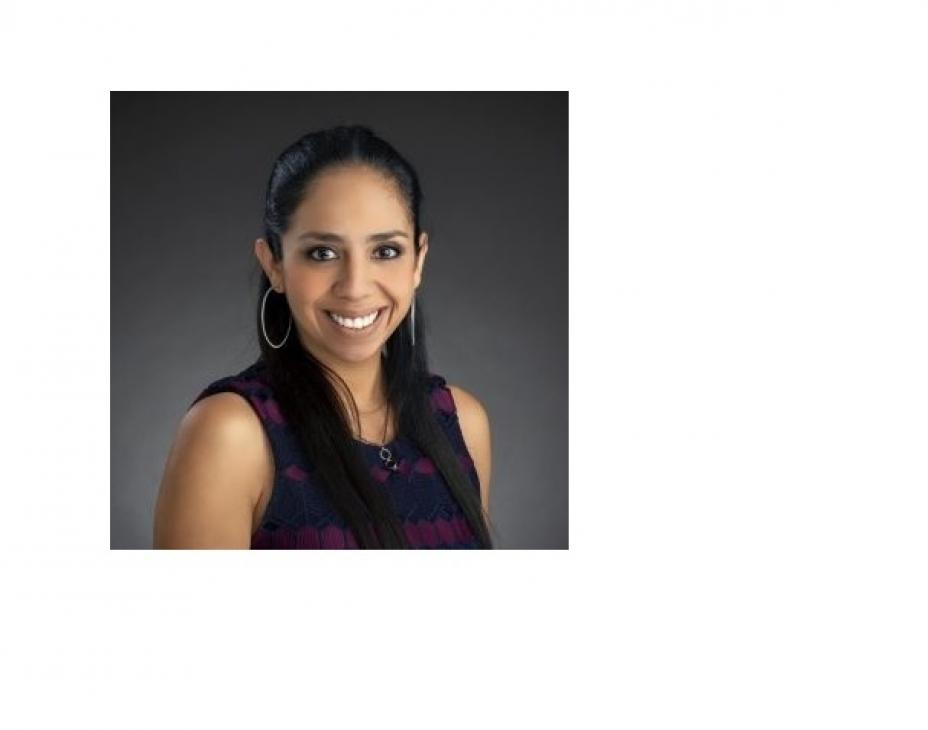 Headshot of Dr. Liliana Vasquez against a dark gray background. She's wearing a black shirt with shoulder-length black hair and is wearing hoop earrings.