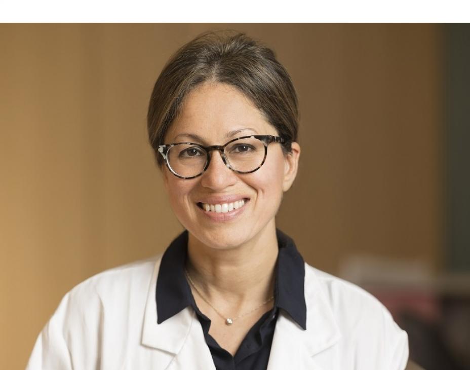 Headshot of Dr. Shanu Modi in a clinical sitting wearing a white coat, glasses, and brown hair. She is smiling facing forward.