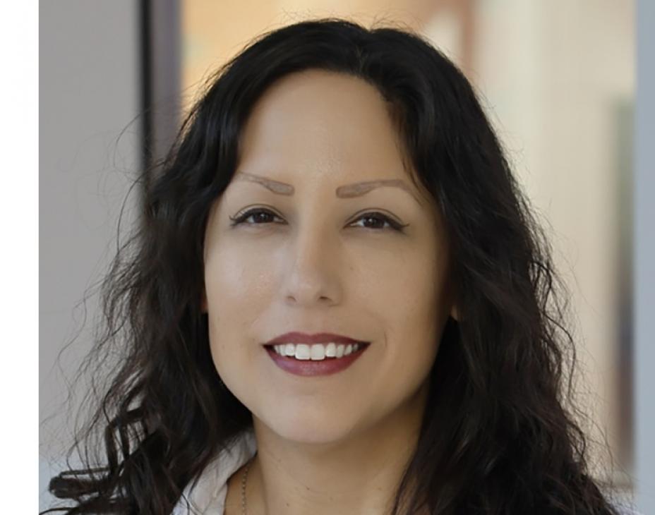Headshot of Dr. Dionisia Quiroga. She is smiling facing forward in a clinical setting and has dark-brown hair at shoulder-length.