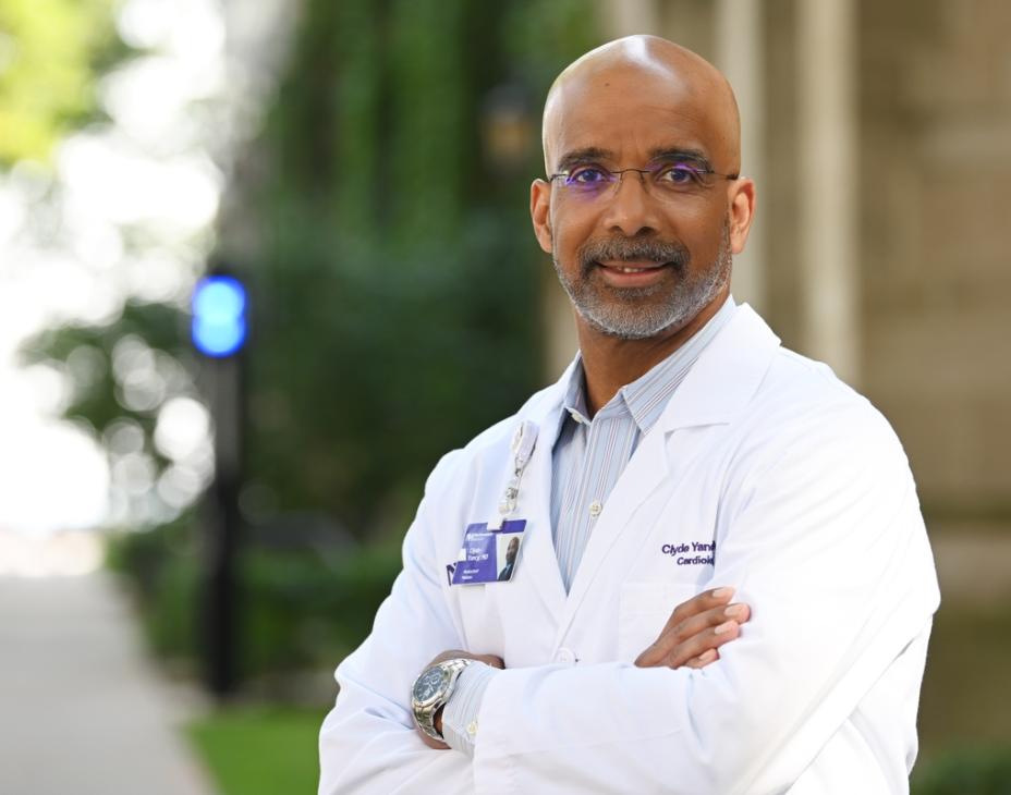 Dr. Clyde Yancy in a white coat, arms crossed, standing outdoors and facing forward.