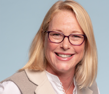 Dr. Amy Peterson headshot. She has shoulder-length blonde hair and is wearing glasses, smiling facin forward against a light-gray background and wearing a white/tan shirt.