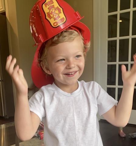 Leo smiling with his arms up around his firefighter helmet.