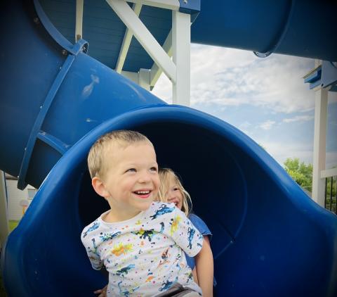 Leo laughing and smiling while sliding out of a blue slide.
