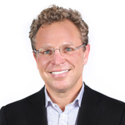 Alexander Casdin, wearing glasses, a black blazer with light-blue shirt. Smiling facing forward.