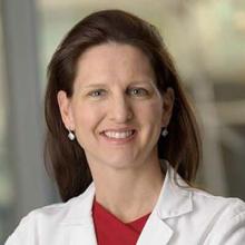 Dr. Kathryn Beal headshot. She is wearing a white coat with a red shirt underneath and has long brown hair. She is smiling facing forward.