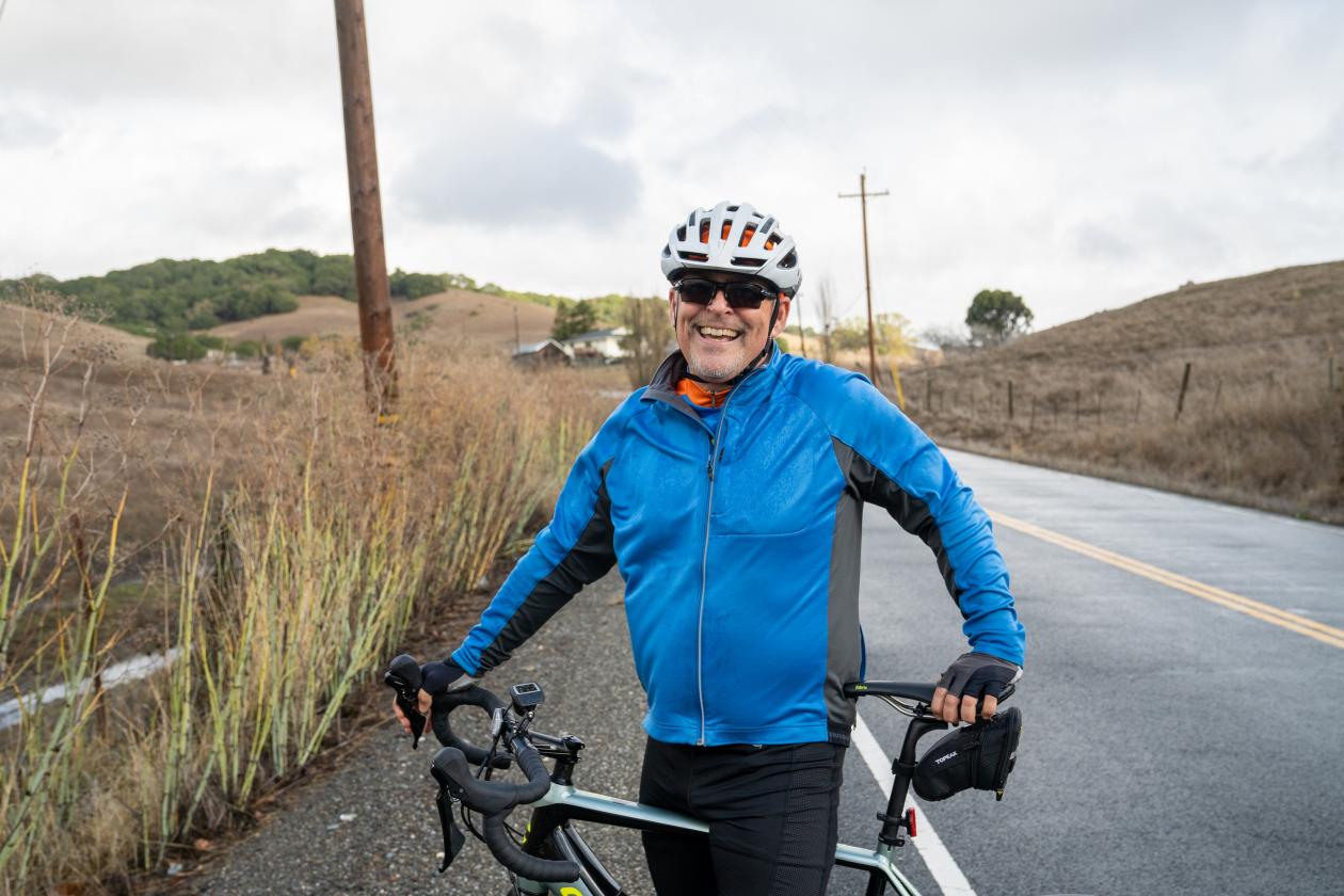 Mark Crafts in an orange shirt, silver helmet, black sunglasses, and electric-blue face-mask