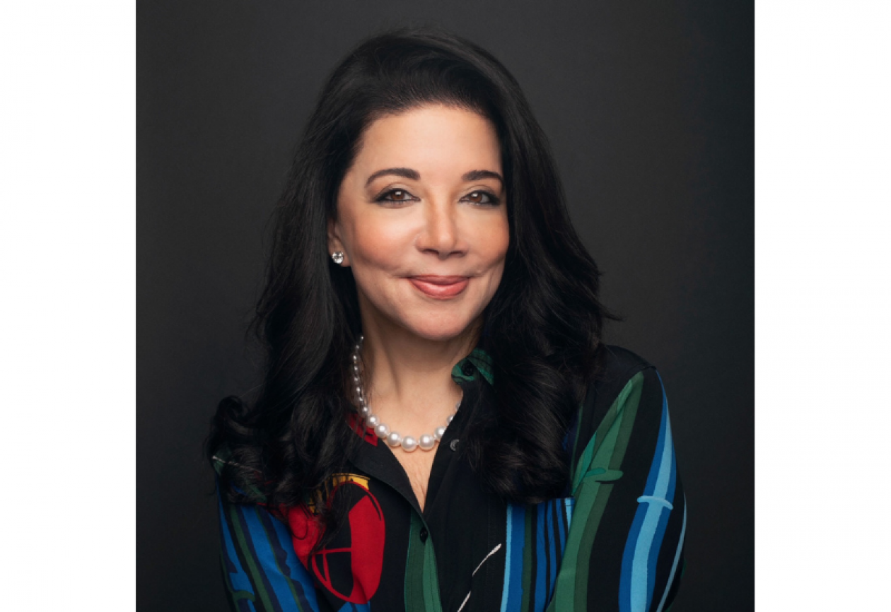 Headshot of Conquer Cancer Board member Deanna B. van Gestel. She is shoulder-length jet-black hair and is smiling facing forward against a dark-gray background. She is wearing a pearl necklace and multicolored blouse.