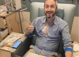 Dave Thau in a clinical setting, smiling and holding a thumbs-up. He has a monitor attached to his chest and is sitting, with a laptop.