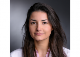 Dr. Ana Garrido-Castro headshot. She is smiling facing forward against a dark gray background, with shoulder-length brown hair.