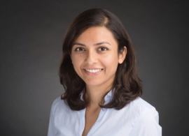 Dr. Sahaja Acharya headshot. She is smiling facing forward against a dark-gray background.