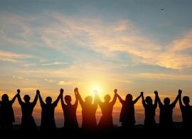Silhouettes of people holding hands up and looking into the sunset