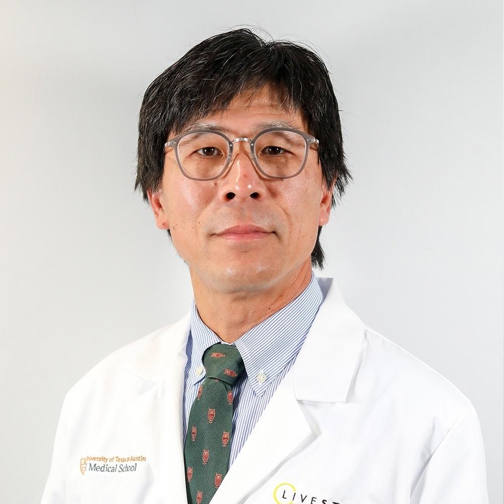 Dr. William Matsui, wearing a white coat and glasses against a gray background. He has black hair and is facing forward.