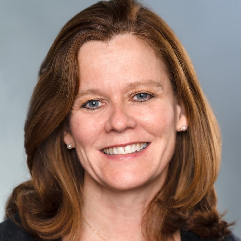 Dr. Ann Partridge headshot. She is smiling facing forward against a gray background. She has shoulder-length auburn hair and is wearing a black sweater.