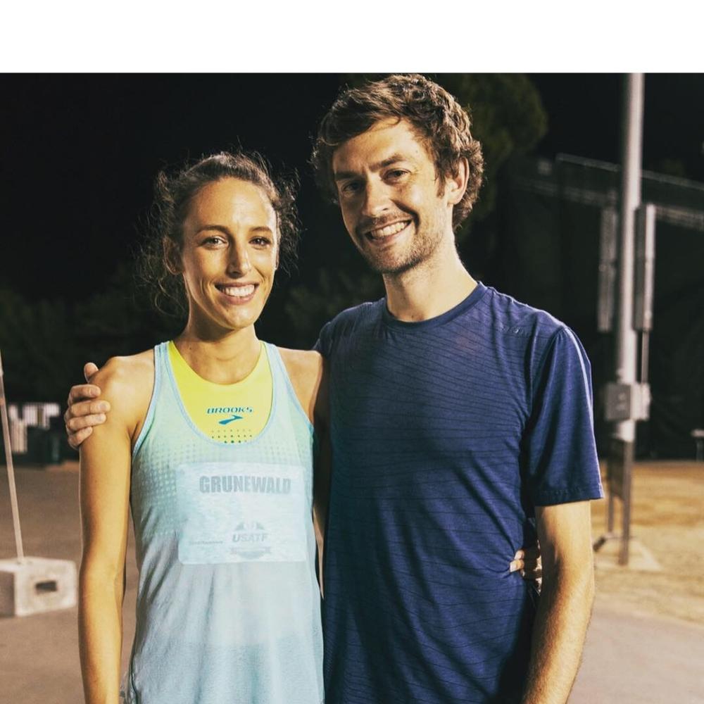 From left to right: Gabe and Justin Grunewald standing next to each other smiling, wearing athletic clothes in a track and field setting.