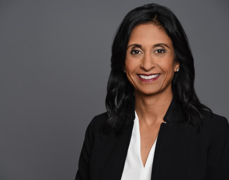 Headshot of Dr. Jyoti Patel. She has shoulder-length black hair, is wearing a black blazer and white blouse, and is smiling facing forward against a dark gray background.