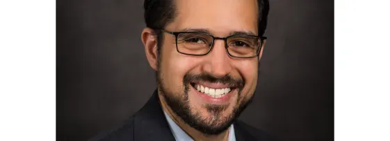 Dr. Pavlos Msaouel headshot; he is smiling facing forward against a dark-gray background.
