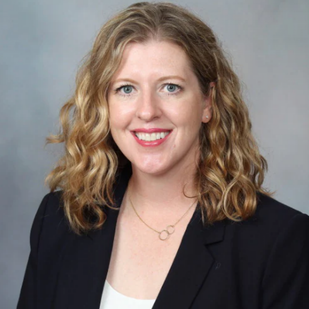 Headshot of Dr. Wendy Allen-Rhoades. She is smiling, facing forward. She is wearing a black blazer over a white shirt, with a smal golden necklace. Her hair is light brown and shoulder-length.