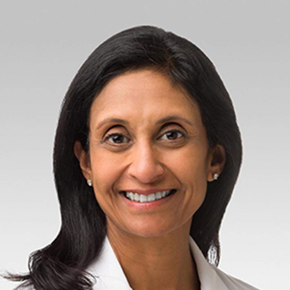 Headshot of Dr. Jyoti Patel. She has shoulder-length black hair, is wearing a white coat, and is smiling facing forward against a gray background.